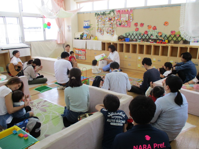 保育参観でおうちの人と一緒に絵本をみる1歳児