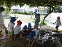 砂場に水を運んで池を作る5歳児