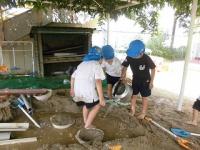 砂場の穴にやかんで水を運ぶ5歳児