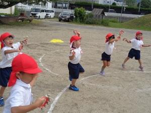 園庭で鈴を持ってリズムをする4歳児