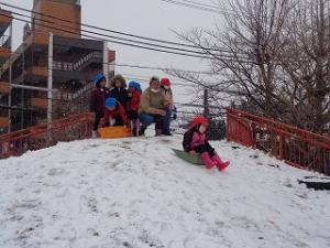 雪の積もったつき山でそり滑りをする園児たち