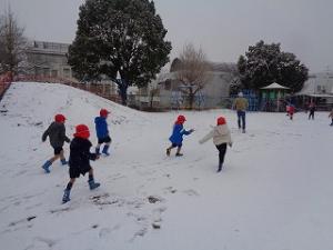 先生をおいかけて雪玉を投げる4歳児