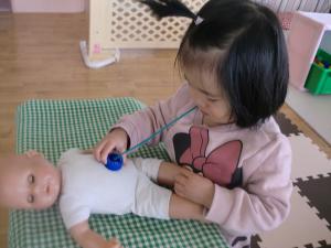 1歳児さんが、ペットボトルのふたを聴診器にして遊んでいます。