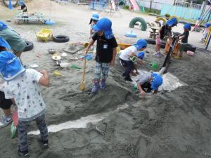 ４歳児が園庭の砂場で水を使って遊んでいます。