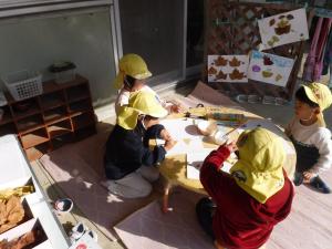 5歳児がドングリや落ち葉・木の実などを使いボンドで貼り絵製作をしています。