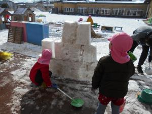 雪を固めて塔をつくる3歳児と先生