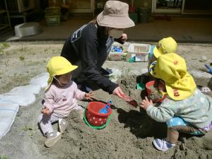 1歳児がスコップで砂をすくっています。
