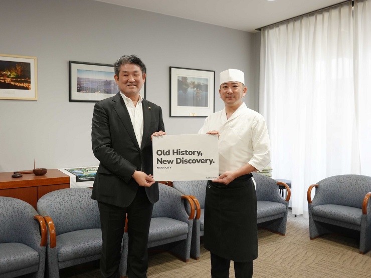 英語スローガンのボードを手に持つ仲川げん奈良市長(左側)と西原理人さん(右側)