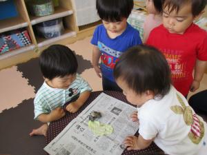 新聞の上にのったかたつむりを見ている子ども達