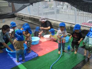 子どもがタライに手をつけたりして水遊びをしている。