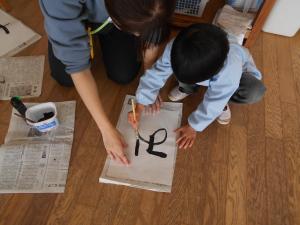 先生と一緒に書き初めをしている子ども