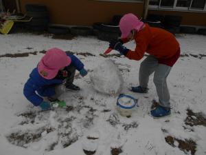 5歳児が友達と一緒に雪だるまをつくっています
