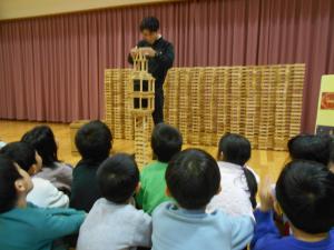 先生がカプラを積む姿を真剣に見る子ども達