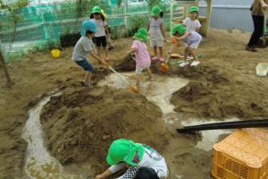 砂場に水を流して遊ぶ子ども達