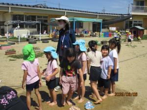 園庭で水たまりに足をつけて遊んでいる子ども達