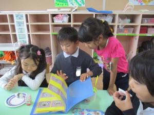 ままごとにお寿司屋さんのメニューを見ている子ども達