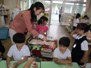 ままごとの料理を運ぶ先生と子ども