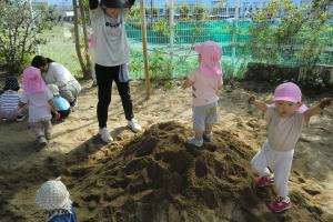 先生と砂の山に登ったり下りたりして遊ぶ子ども