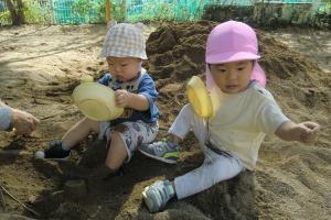 お皿を使って砂場で遊ぶ子ども