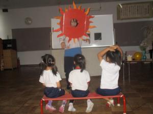 太陽のお面をかぶった先生の話を聞いている子ども
