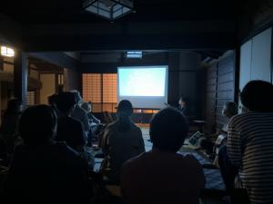 旧細田家住宅の部屋でスクリーンを見ながら講師の先生の話を聞いている様子
