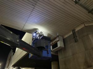 夜間、歩道橋の下から高所作業車を使って点検作業をしている画像