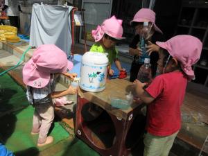 4人の子どもが色水を容器に入れて遊んでいます、