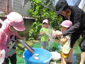子どもが保育者と一緒に水鉄砲で遊んでいます。