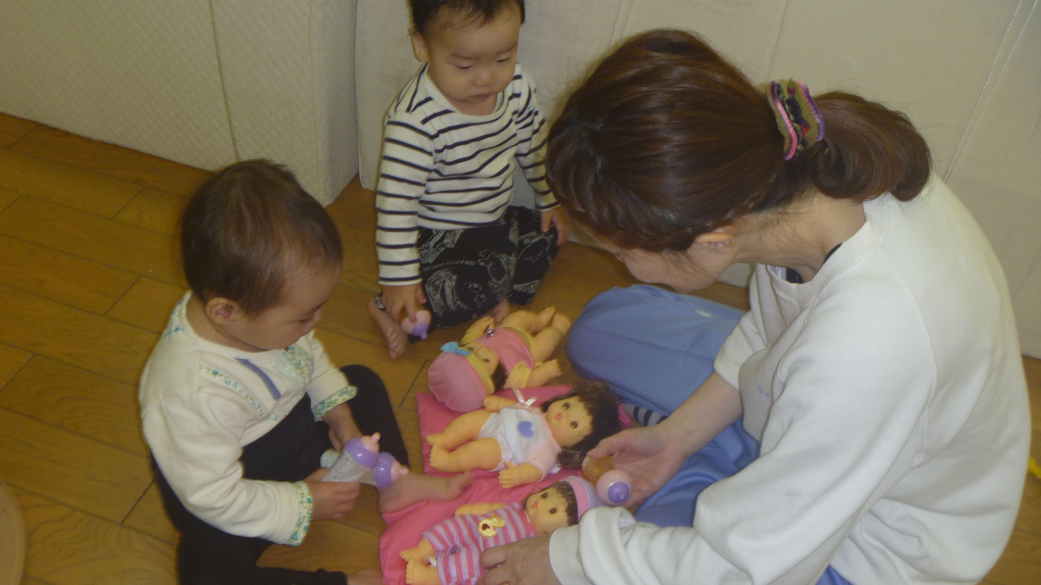 0歳児が保育者と一緒に赤ちゃん人形で遊んでいるところ