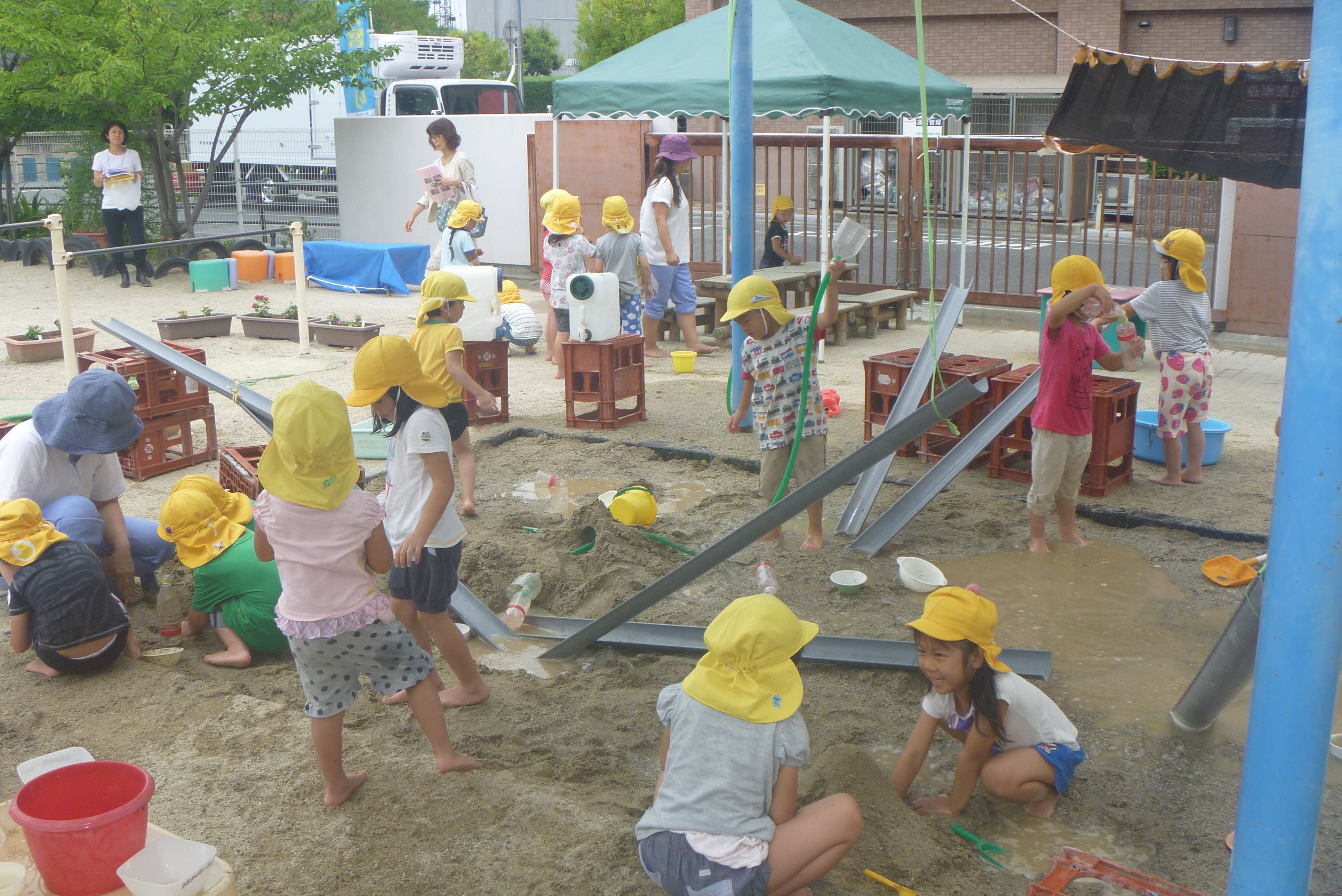 幼児が園庭の砂場でさまざまな仕掛けを作りながら遊んでいるところ