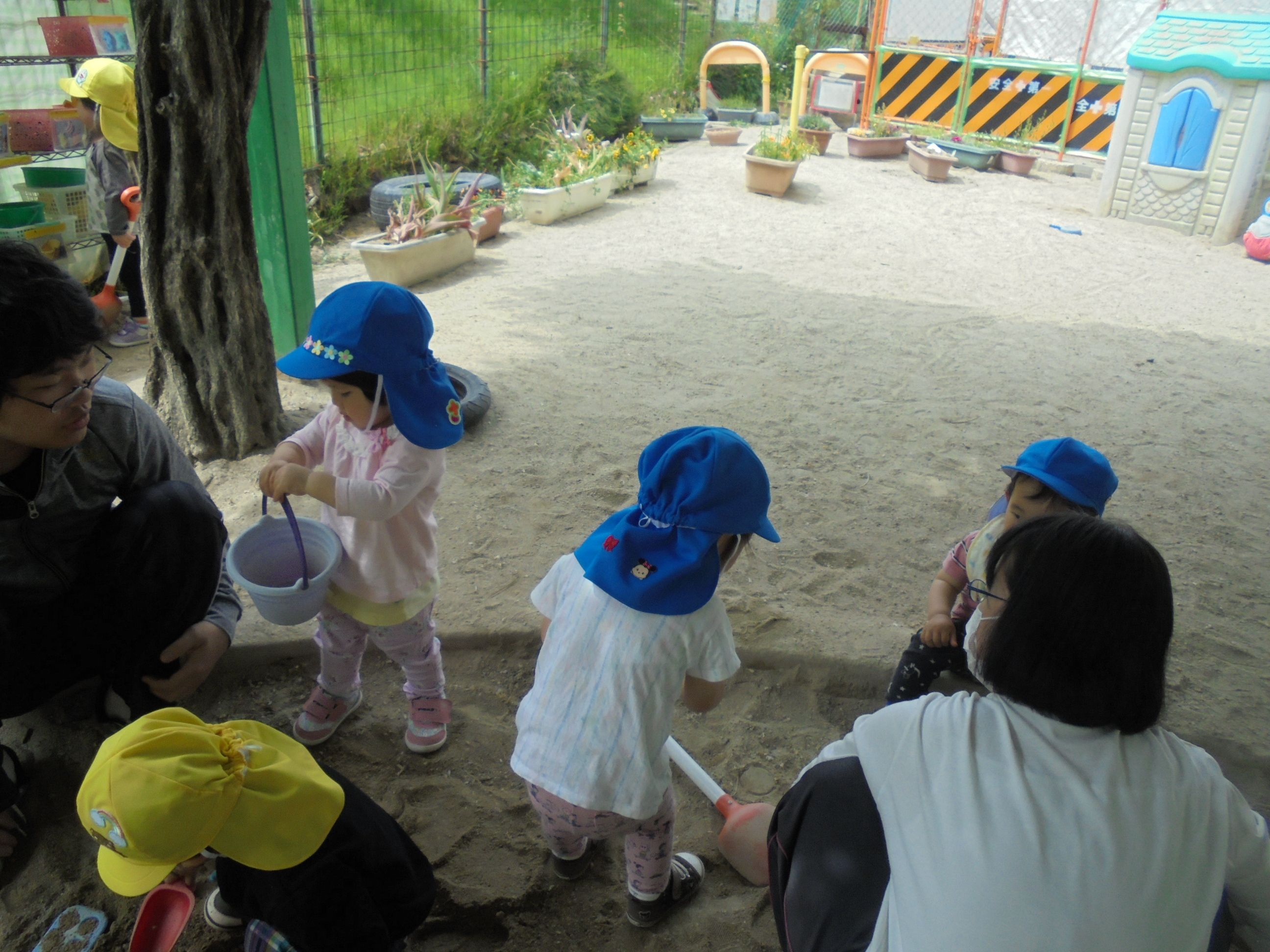 1歳児クラスの子ども達が先生と一緒に砂場遊びをしている様子
